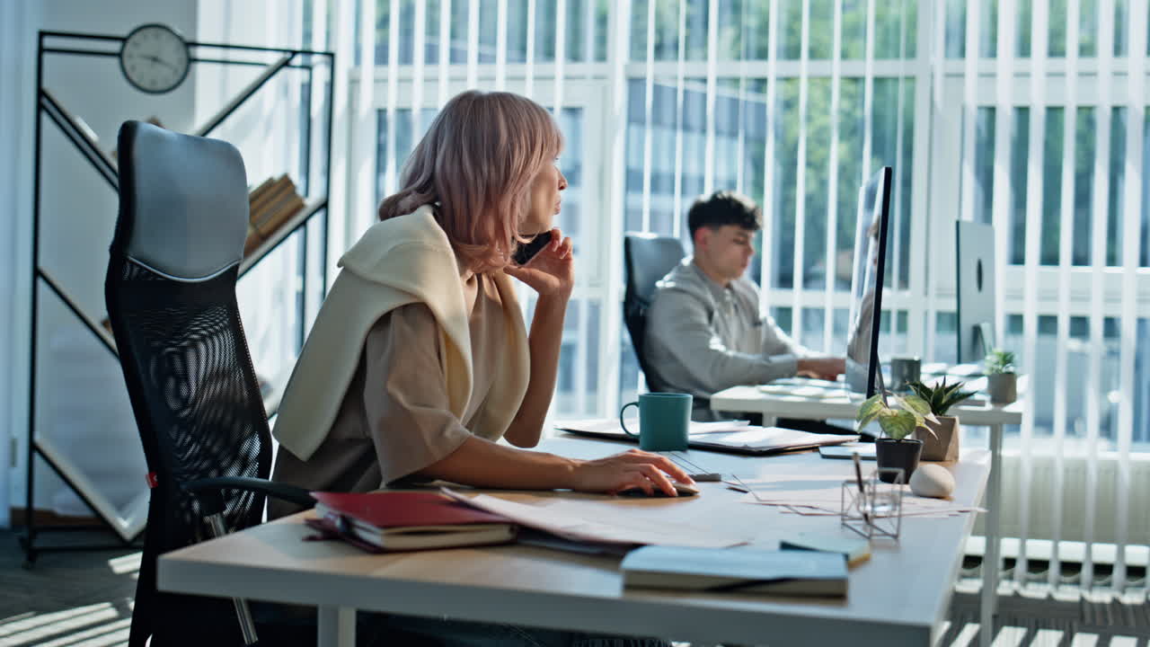 Travl administrator taler i mobiltelefon i et kontor i åbent rum tæt på. Kvinde ringer