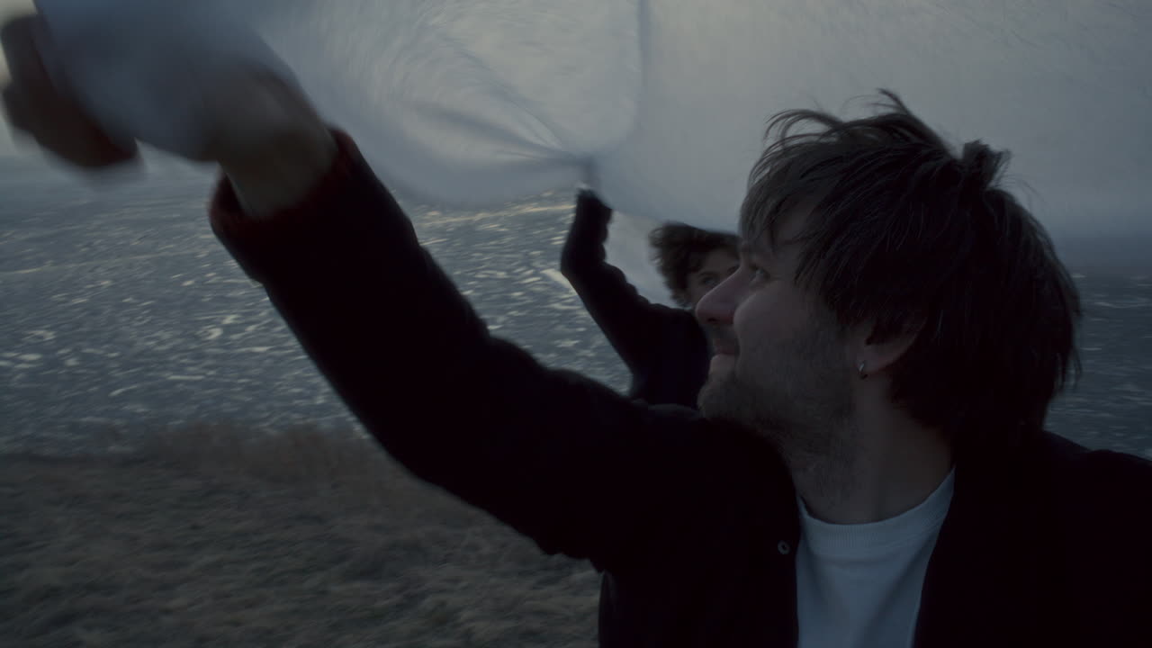 Happy Couple Lifting White Fabric over Their Heads on Frozen Lake Shore