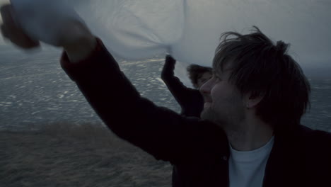 happy couple lifting white fabric over their heads on frozen lake shore