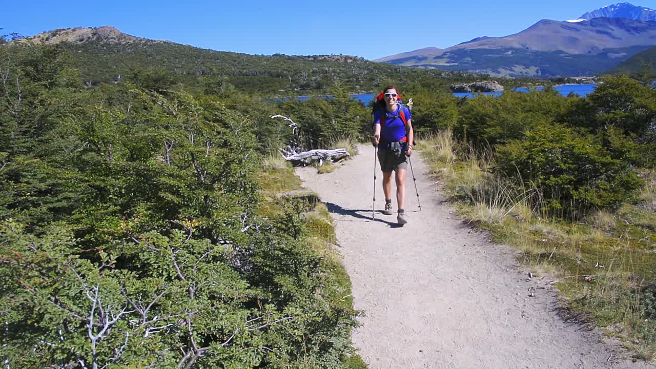 mujer joven caminando por un sendero y saludando con las manos en patagonia, argentina