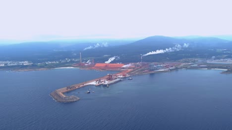 aerial drone shot over large ship unloading raw materials by the port of the aluminium factory in san ciprián, morás, xove, lugo, galicia, spain on a cloudy day