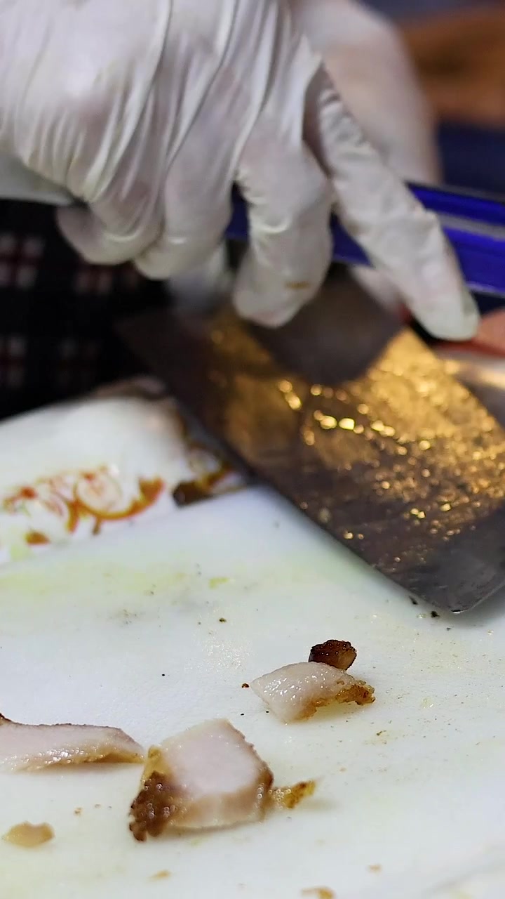Chef slicing pork at a bustling food stall