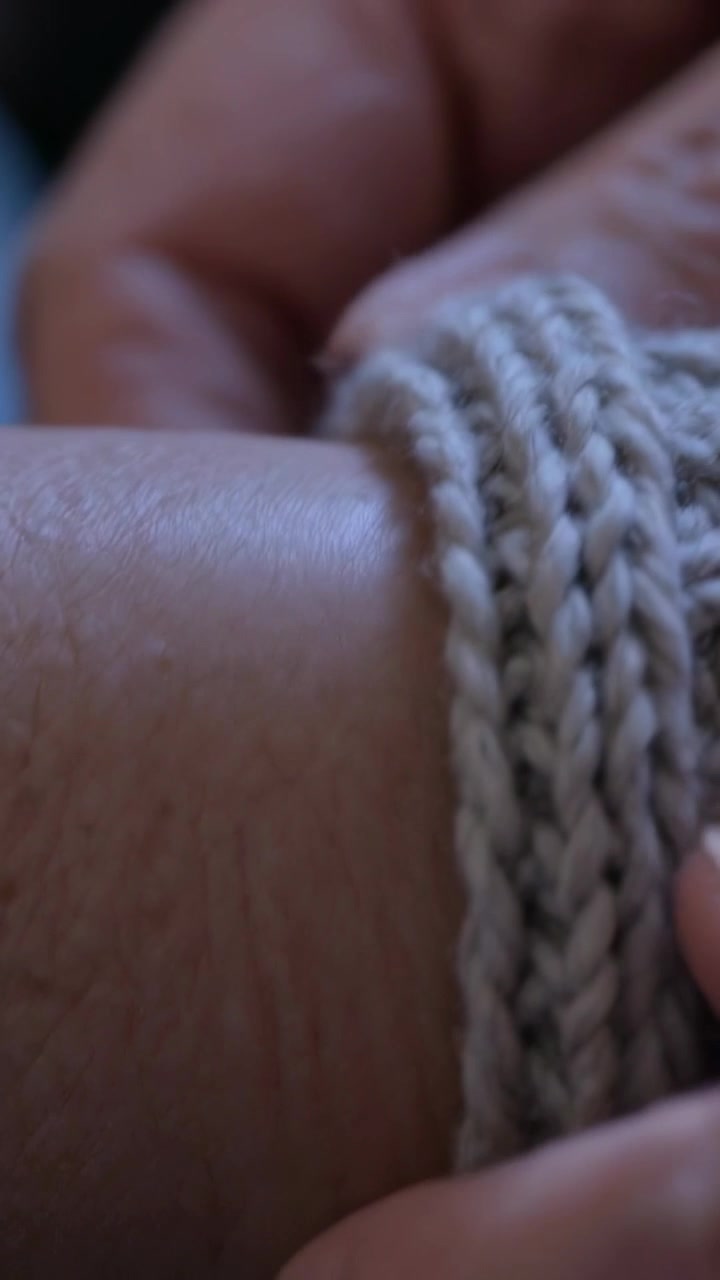 Video verticale: Mani che allungano e posizionano un polsino in maglia color crema sull'avambraccio a casa, rimboccando per tenersi al caldo.