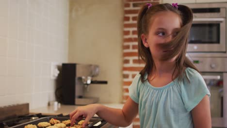 chica caucásica comiendo galletas horneadas en la cocina en casa