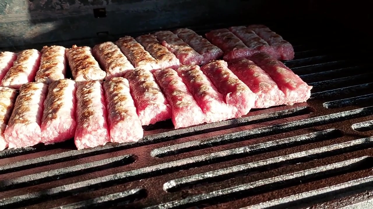 Rotoli di carne macinata chiamati cevapcici che grigliano su una griglia di ferro calda riscaldata a carbone.