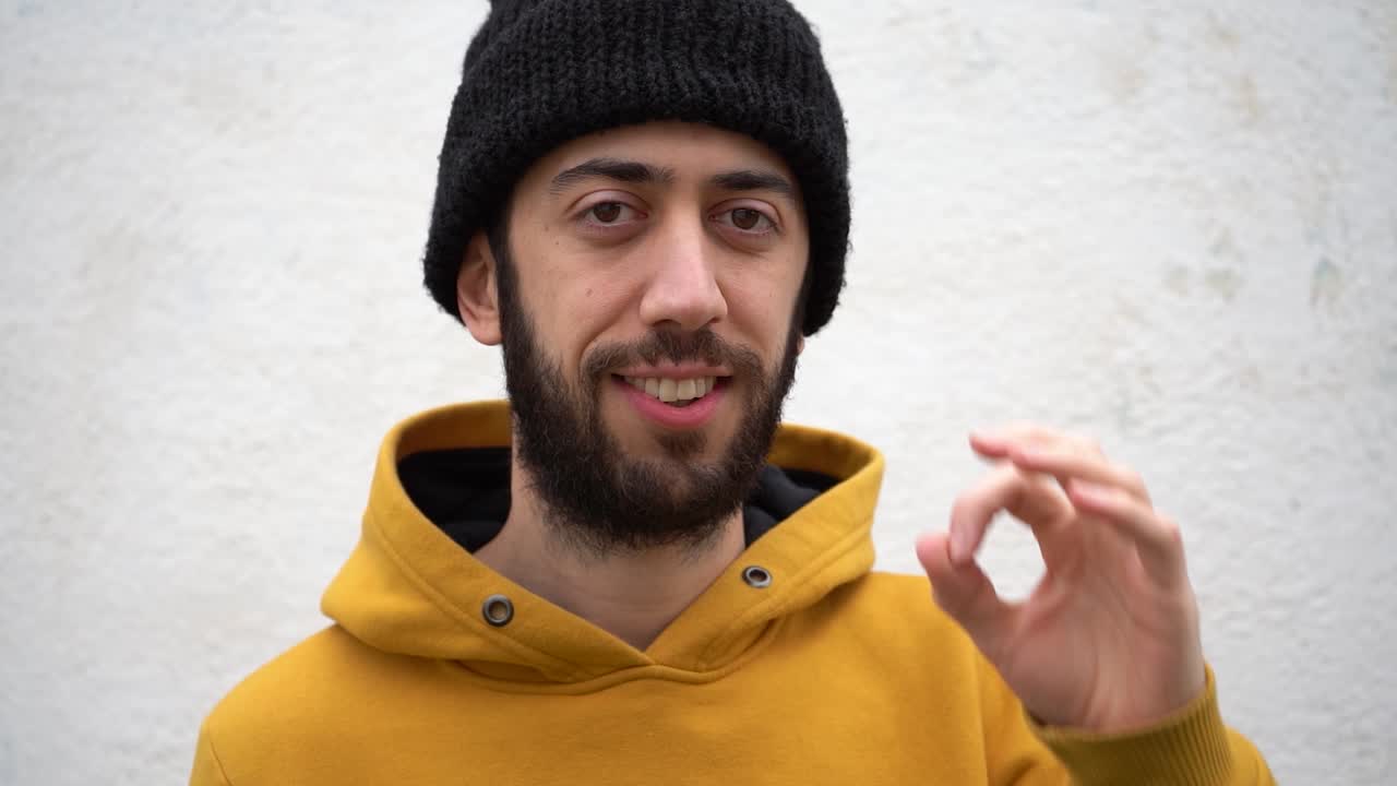 Man In Yellow Hoodie And Beanie Hat Doing An Okay Sign While Smiling In Front Of The Camera. Close-up Shot
