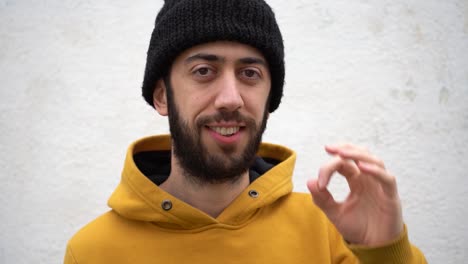 man in yellow hoodie and beanie hat doing an okay sign while smiling in front of the camera. close-up shot