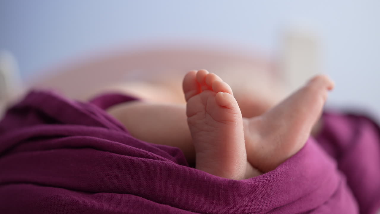 Primo piano di piedini di neonato avvolti in un tessuto viola