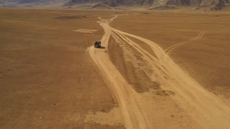 aerial dolly of van driving through steppe on dust road towards mountains in daytime, mongolia