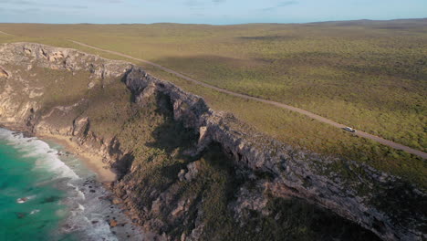 aerial view following a car and a trailer, driving on the coastline of kangaroo island, australia, sunny day - pull back, drone shot