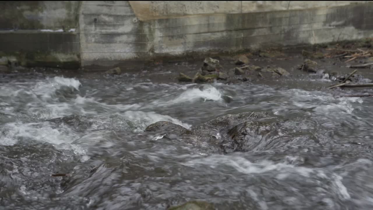 Fast current of shallow river flowing over rocks below concrete sluice