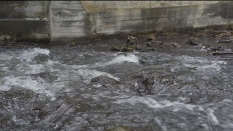 corriente rápida de un río poco profundo que fluye sobre las rocas debajo de una esclusa de hormigón