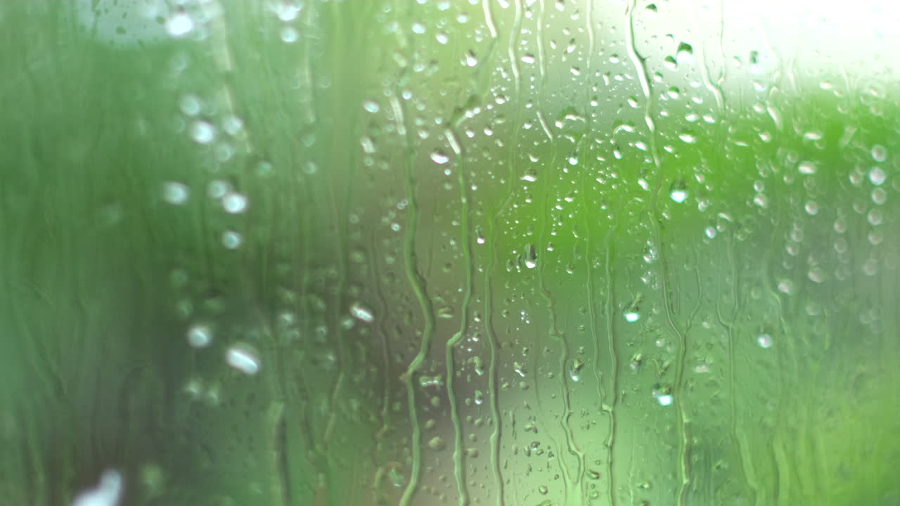 Raindrops splutter against outside of window, shallow focus and green background