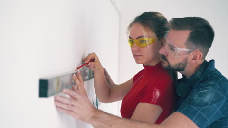 woman with boyfriend checks wall level in light room closeup