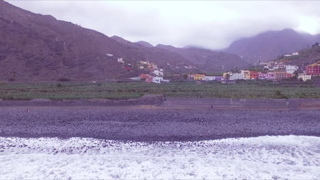 Aerial-view-of-Hermigua-beach,-valley,-banana-plantation,-colorful-houses-and-mountains-in-hermigua-valley,-North-of-La-Gomera,-Canary-Islands,-Spain-on-a-cloudy-day