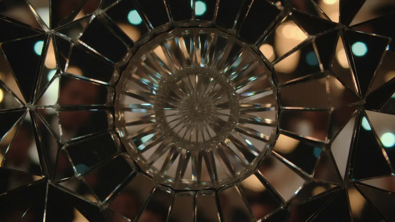 Shifting light revealing crystal disc refracting amber and teal lights in lounge, blurred figures