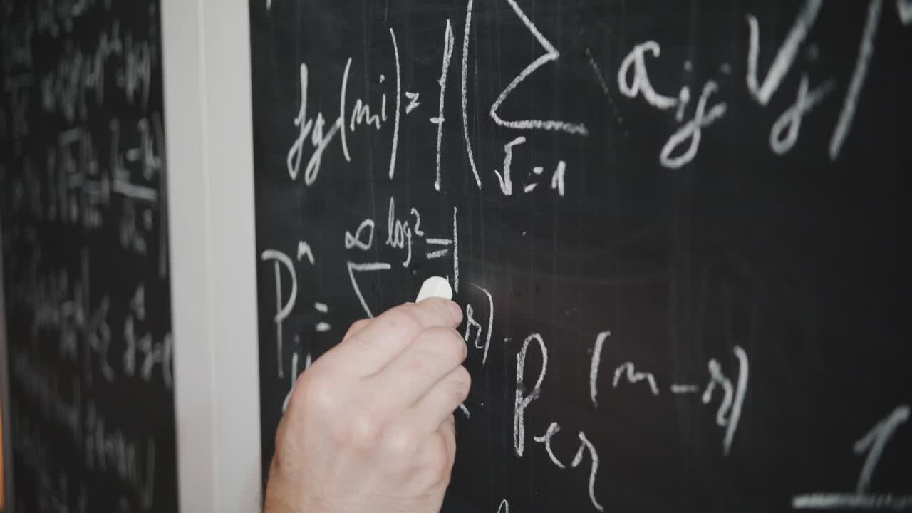 A close-up shot of a scientist's or teacher's hand writing a complex math or physics equation on a blackboard. Concept of education, academia, research, and problem-solving