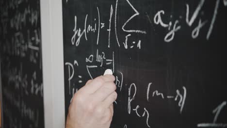 a close-up shot of a scientist's or teacher's hand writing a complex math or physics equation on a blackboard. concept of education, academia, research, and problem-solving