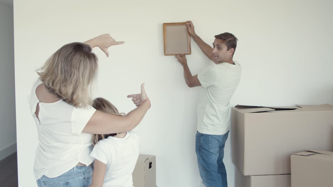 Bambina con sua mamma che aiutano il papà a scegliere il posto per un quadro