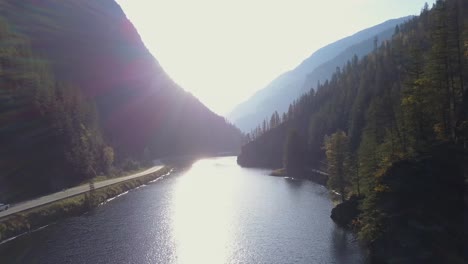 Relaxing-low-flight-along-a-mountain-lake-directly-into-the-sun,-with-road-and-railway-2-of-2