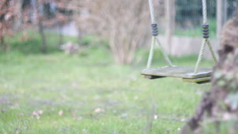 Wooden-Tree-Swing-in-a-Garden-Gently-Moving,-No-People,-Shallow-Focus