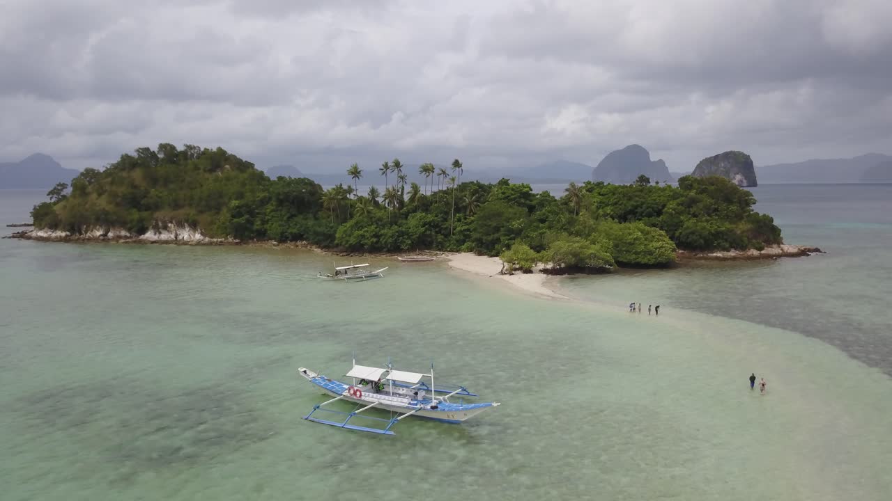 Ripresa aerea con drone che avanza verso un banco di sabbia di un'isola tropicale a Palawan, Filippine, con persone che camminano lungo la sabbia bianca in una pittoresca destinazione per il tour delle isole