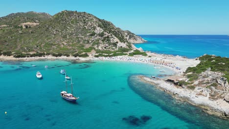 punta molentis beach in villasimius, sardinia - boats and tourists in turquoise blue sea and small white sandy beach - aerial 4k circling