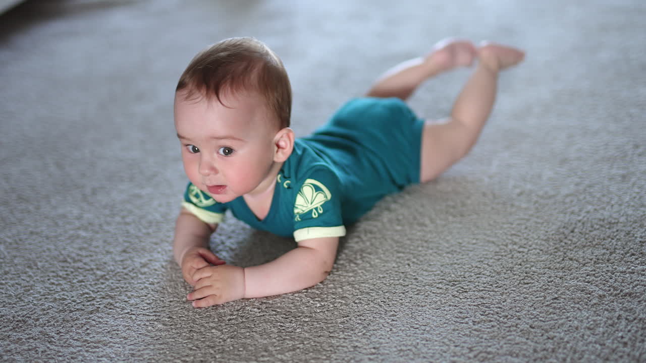 Nice baby boy lies on the floor looking up to the camera with surprise. Funny little child banging arms and legs by the floor.