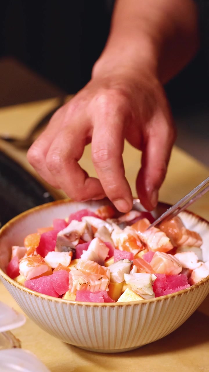 Close-up shot of a chef's hands meticulously placing diced seafood into a chirashi bowl