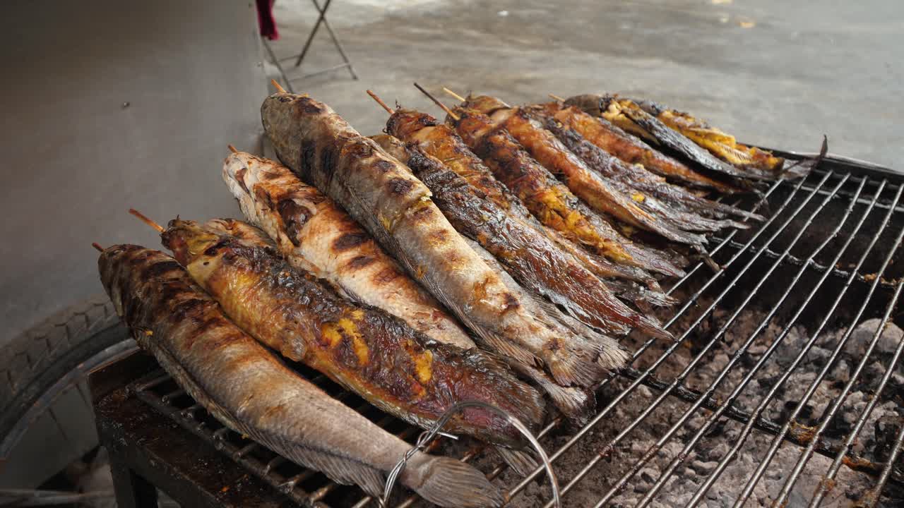 Close-up shot of fish grilling over open flame on a street in Phnom Penh. The charred, succulent fish captures the essence of Cambodian street food in vibrant daylight