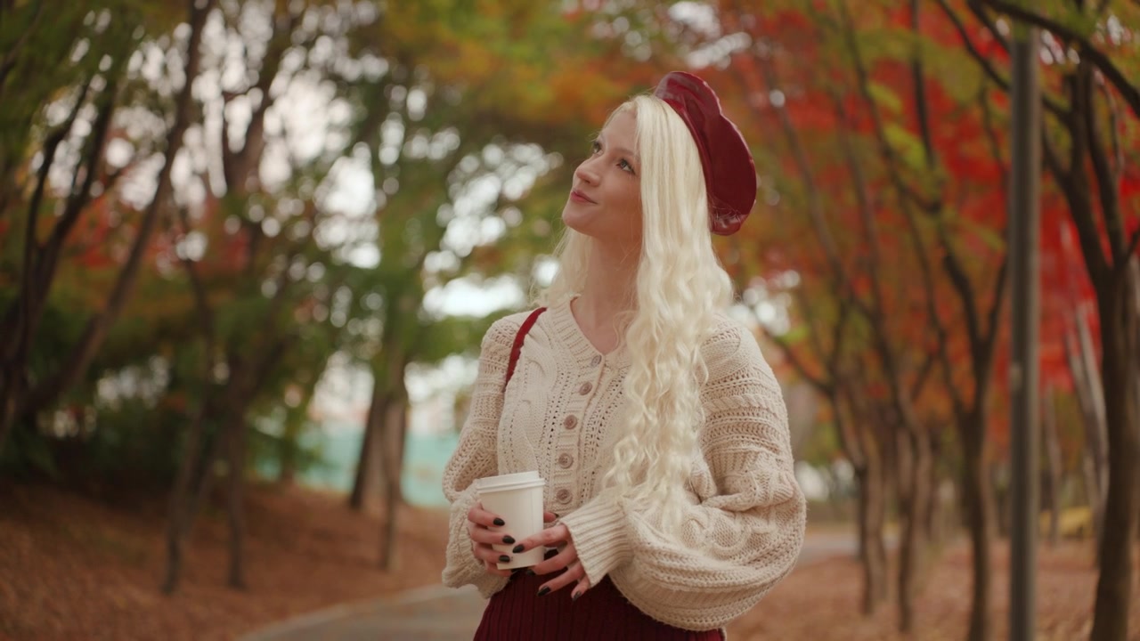 Europeisk kvinne går med en kopp kaffe i Yangjae Forest Park, omgitt av høstløvverk mens hun beundrer trærne, sakte film med medium sporing