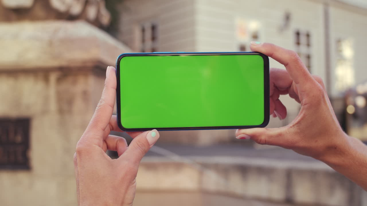 Hands holding a smartphone with a green screen outdoors