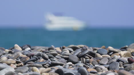 pebbles on sunny beach with blurry ship at sea