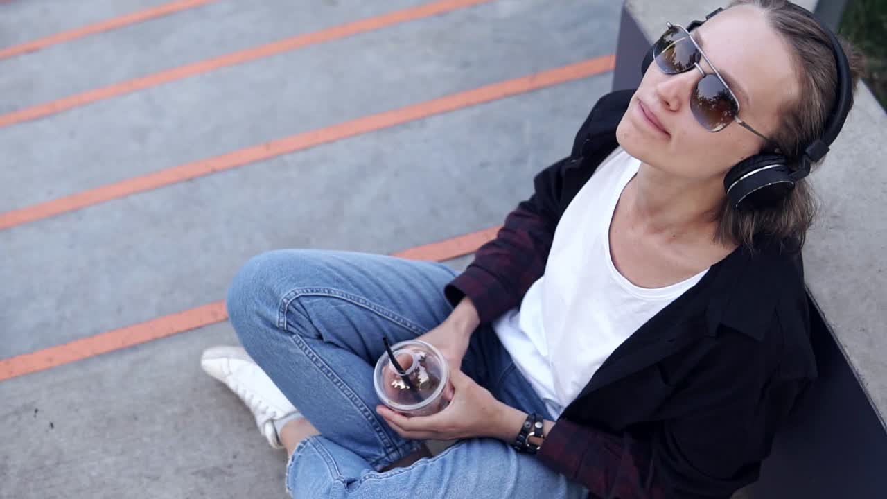 imágenes de ángulo alto de una hermosa chica sentada en el suelo o el asfalto bebiendo cóctel del vidrio transparente con un