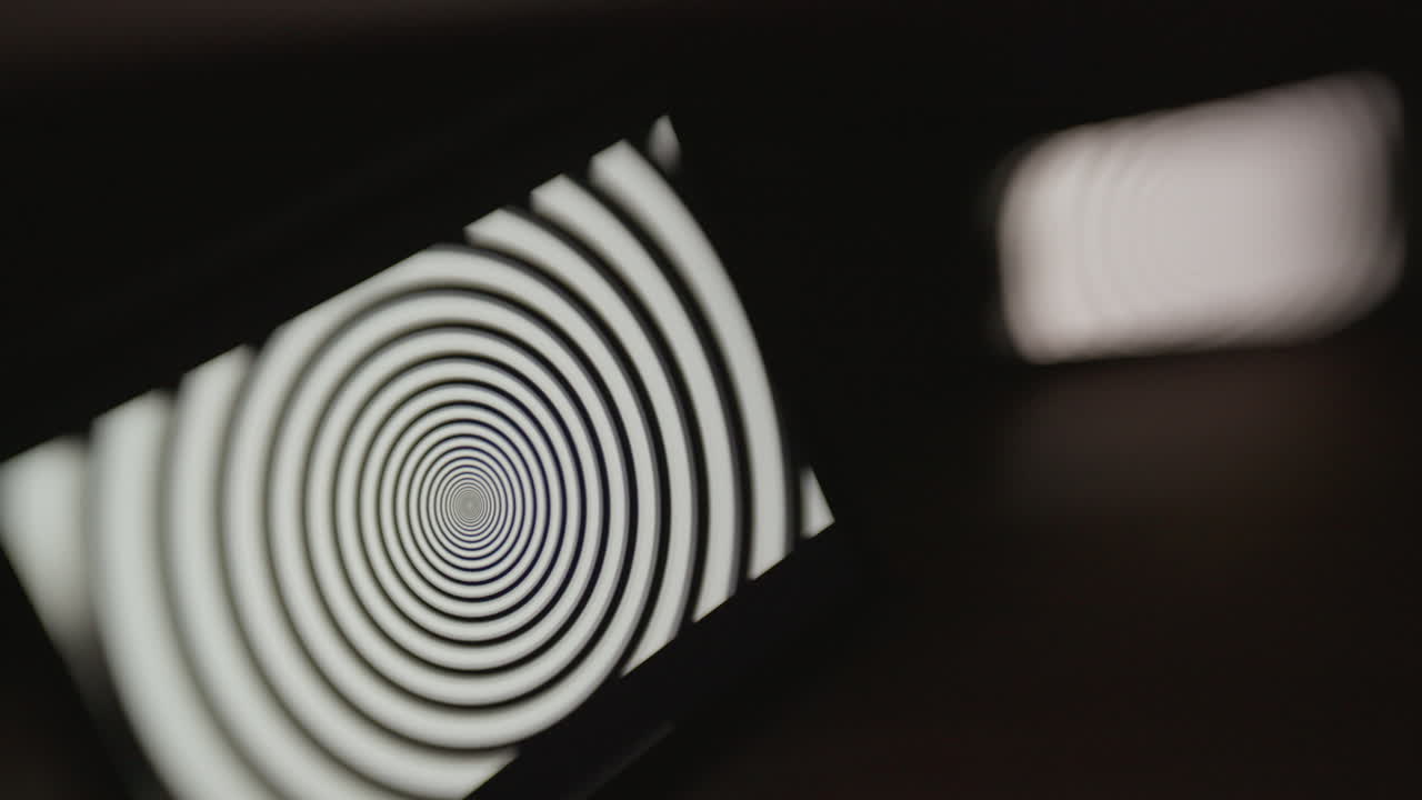 A tablet device in focus and a mobile phone out of focus in a dark room, both displaying a hypnotic spiral pattern