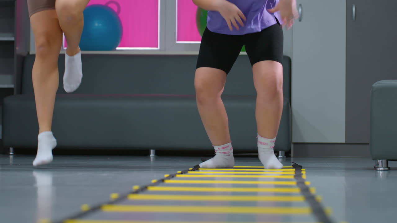 여성 운동 세션의 낮은 각도 뷰, 참가자들이 균형과 체력 훈련을 위해 민한 사다리를 통해 통제된 점프를 수행하는 동안 안정성과 조정에 초점을 맞추고 있습니다.