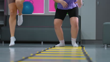 vista de ángulo inferior de la sesión de entrenamiento femenina que se centra en la estabilidad y la coordinación mientras los participantes realizan saltos controlados sobre la escalera de agilidad para el equilibrio y el entrenamiento de resistencia