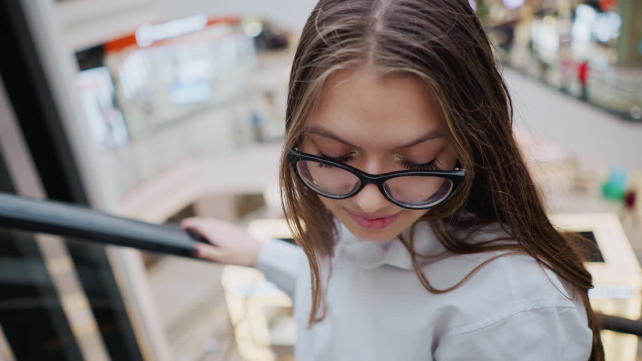 Close up of lady in glasses on an escalator in a busy mall, capturing her focused and observant expression amidst the bustling environment