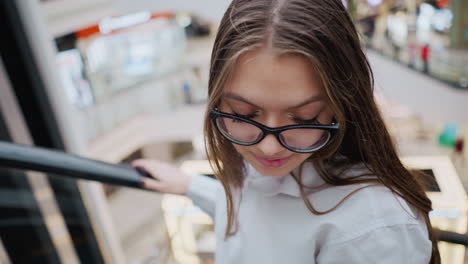 close up of lady in glasses on an escalator in a busy mall, capturing her focused and observant expression amidst the bustling environment