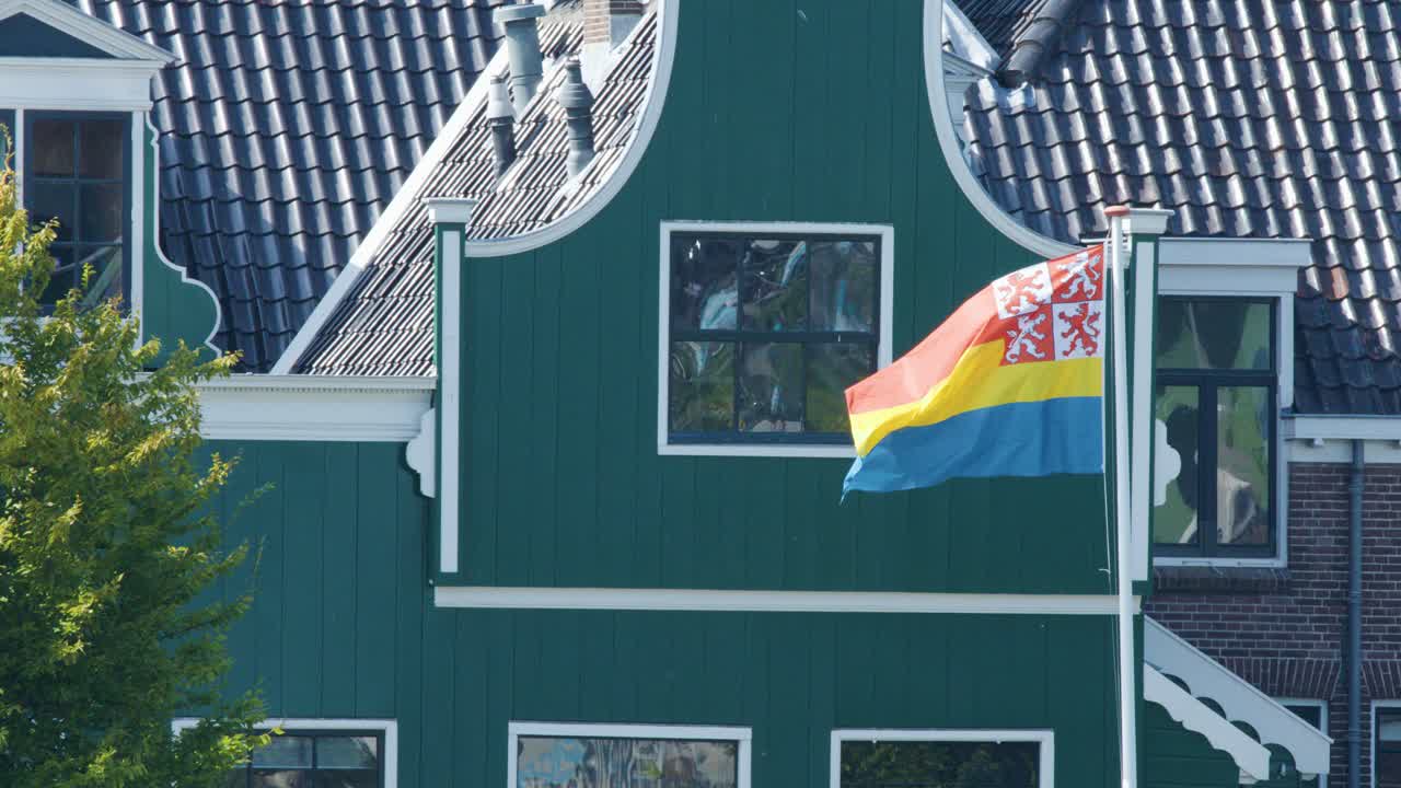 Provincial flag flutters in wind beside traditional green Dutch house, daylight, steady camera