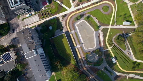 Drone-top-down-rotating-view-above-Park-Centralny,-Gdynia-Poland,-long-shadows-cast-on-grass-from-buildings