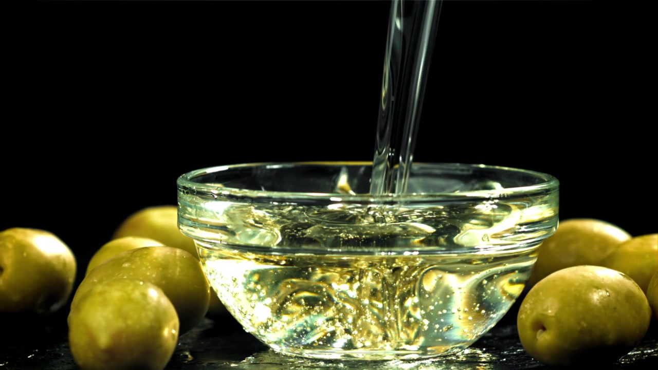 Olio d'oliva fresco versato in una ciotola di vetro con olive verdi