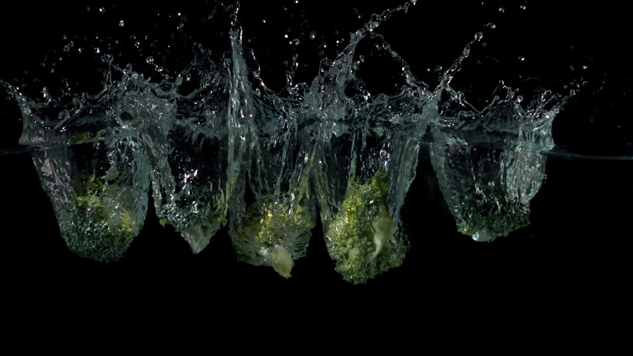Broccoli pieces falling in water on black background