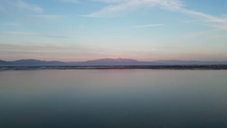 aerial: forward drone flight during sunrise along a coastline with mountain backdrop