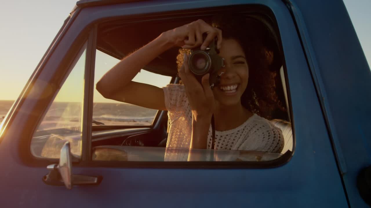 mujer tomando una foto con una cámara digital en una camioneta en la playa 4k