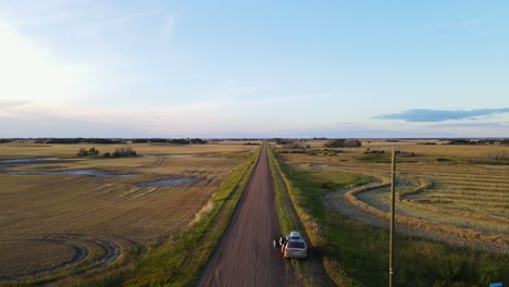 backwards flying drone revealing silver minivan parked along a long and endless dirt road in flagstaff county, alberta