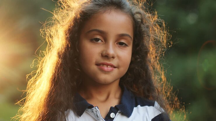 Closeup portrait of little girl looking into the camera outdoors. Sunshine in the background. Blurred background.