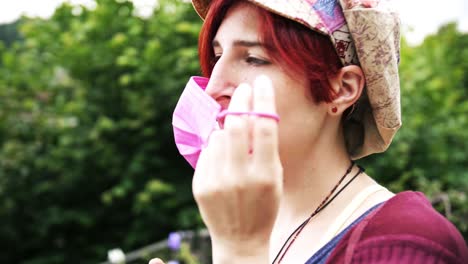 close-up of a young red haired woman pulls off a medical pink face mask with green nature background