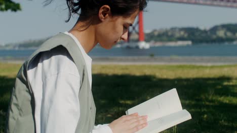 young woman reading in a park by the river