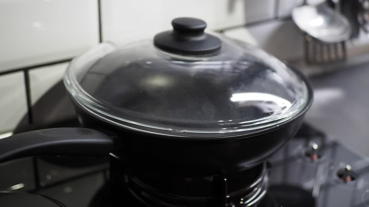 Close-up of a black pan with a glass lid on a stovetop